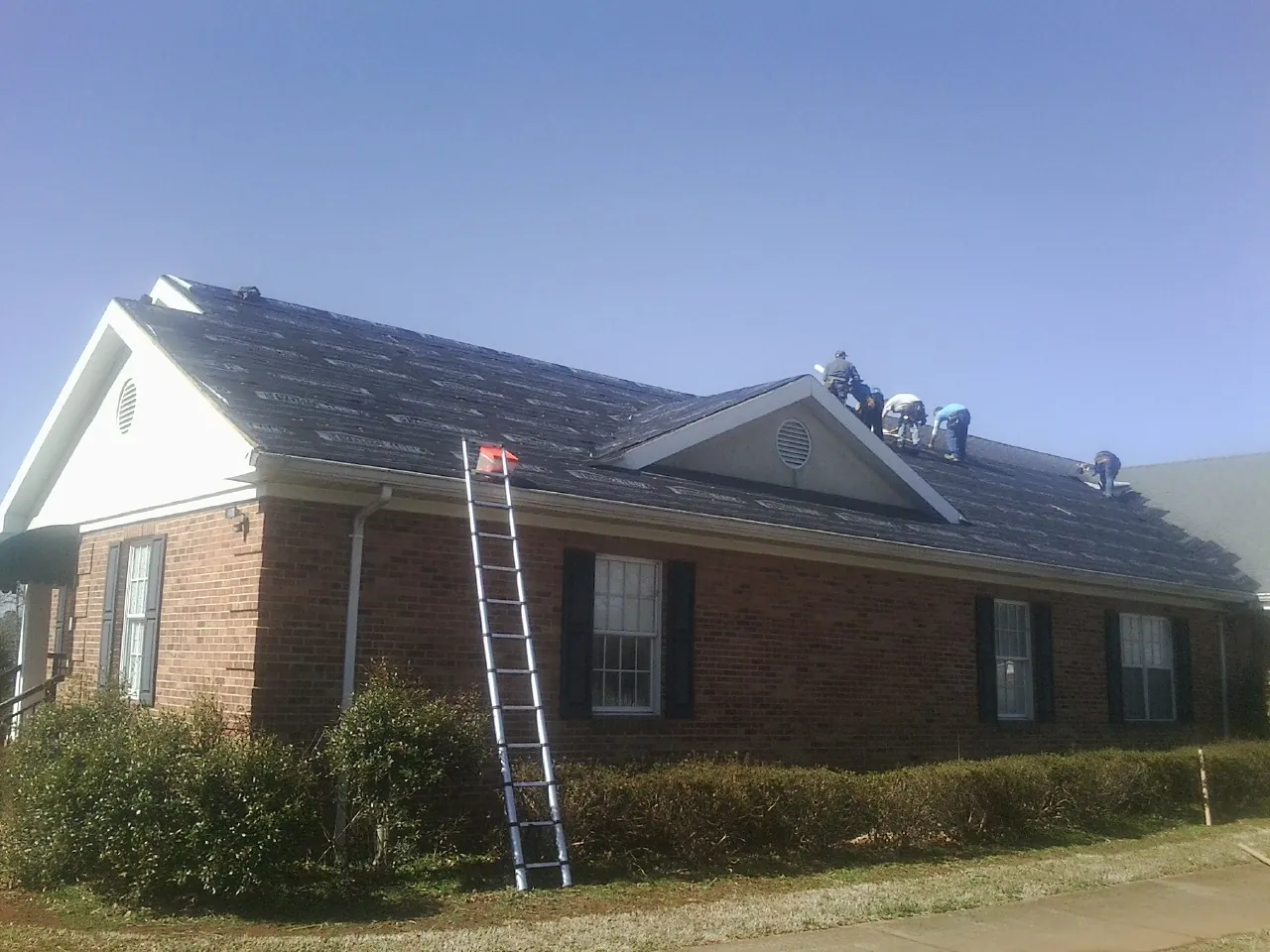 Crew tearing shingles off a brick ranch roof with a ladder set — Emergency Roof Repair work by our crew in New Windsor